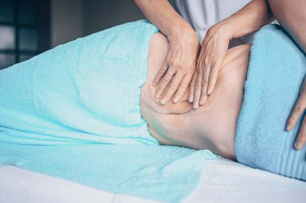 Młoda, nierozpoznana kobieta leżąca na stole do masażu i ciesząca się masażem terapeutycznym. Pielęgnacja ciała, utrata wagi. Masażysta rąk masażysta robi masaż antycellulitowy w klinice spa - Zdjęcie, obraz