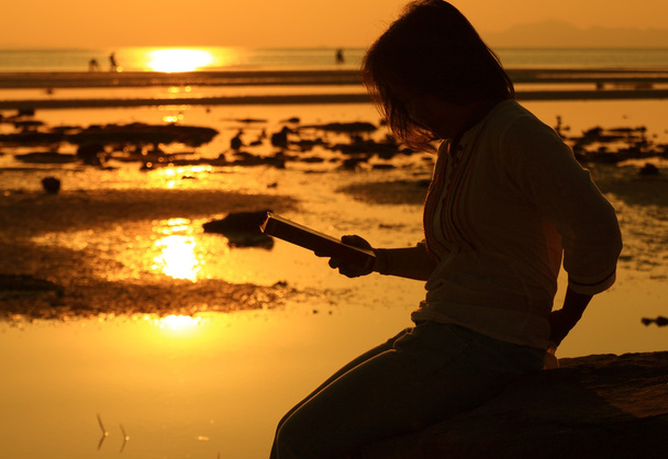 Silueta mujer leyendo libro por playa al amanecer
 - Foto, imagen