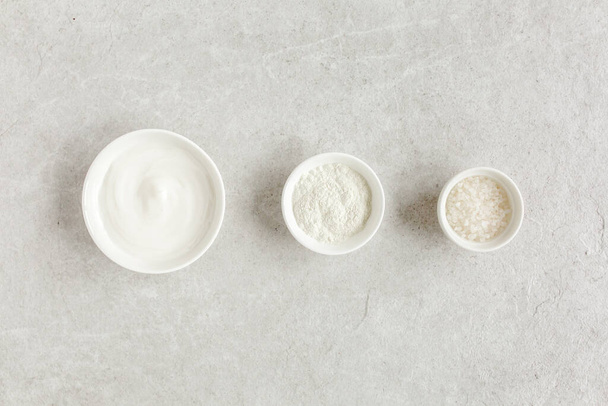 Trois produits cosmétiques naturels dans un bol : crème pour le visage, argile cosmétique, sel de mer sur fond de marbre gris. Concept de soins de la peau.  - Photo, image