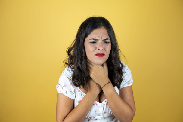 Mooie vrouw over gele achtergrond aanraken pijnlijke nek, keelpijn voor griep, clod en infectie - Foto, afbeelding