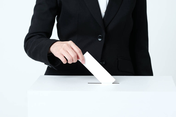 Eine Frauenhand im Anzug steckt Zettel in eine Wahlurne - Foto, Bild