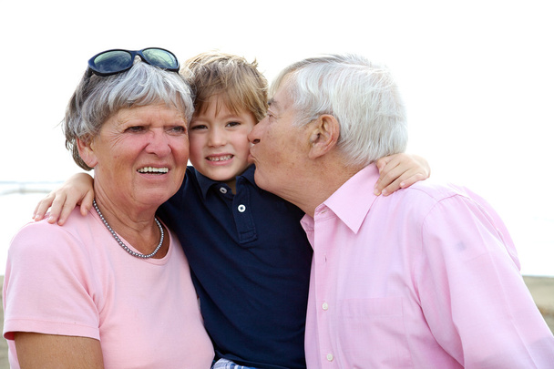 glückliches Kind, das vom Opa geküsst und von der Großmutter umarmt wird - Foto, Bild