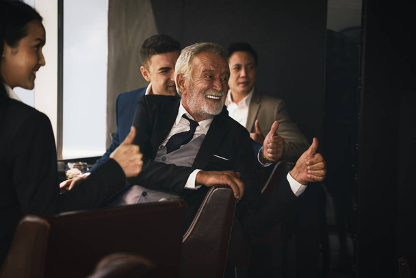 group of business people sitting together near window and having thumb up showing teamwork and confidence  - Fotografie, Obrázek