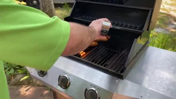 man green shirt with metal tongues cooking stakes and sausages in his outdoor backyard on a propane gas grill - Footage, Video
