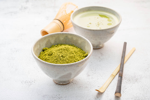 Matcha green tea powder with bamboo matcha whisk brush  setup on white concrete background . - Photo, Image