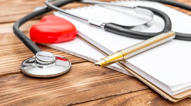 Stethoscope με κόκκινη καρδιά και σημειωματάριο στο τραπέζι. - Φωτογραφία, εικόνα