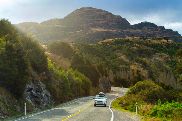Biały samochód biegł po zakrzywionej drodze w dolinie z pięknym światłem po południu w Wanaka, Nowa Zelandia - Zdjęcie, obraz