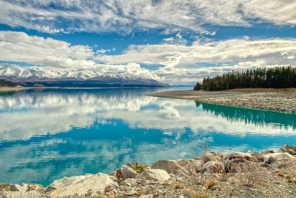 Dağların panoramik manzarası ve göl çam ağaçları Yeni Zelanda 'daki Pukaki Gölü' nün turkuaz suyunu yansıtıyor. - Fotoğraf, Görsel