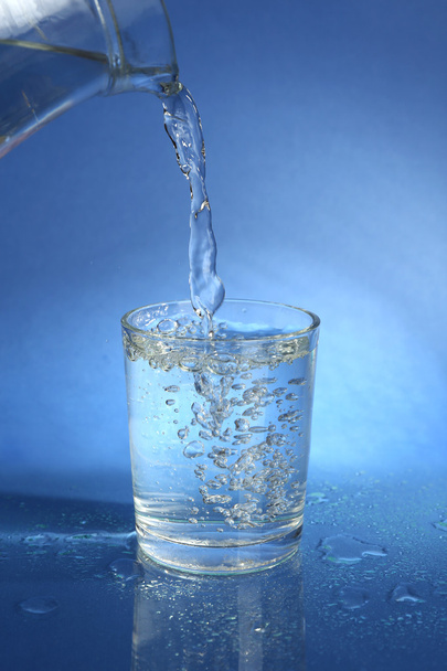 Pour water from pitcher into glass, on dark blue background - Foto, imagen