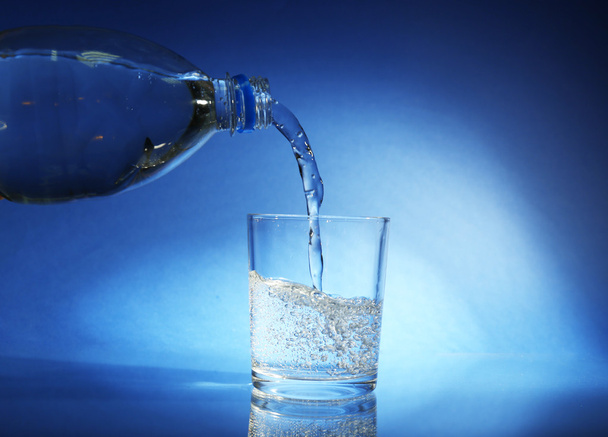 Pour water from bottle into glass, on dark blue background - Foto, imagen