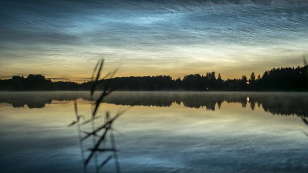 piękny nocny krajobraz z białymi srebrnymi chmurami nad jeziorem, zamazany pierwszy plan, urocze odbicia chmur w wodzie jeziora, letnia noc - Zdjęcie, obraz