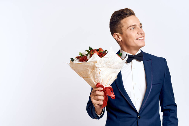 Een elegante man in een klassiek pak met een strikje houdt een boeket bloemen in zijn hand  - Foto, afbeelding