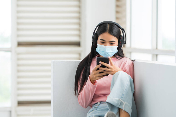 Female college student wearing a mask listening to music at university - Foto, Imagen