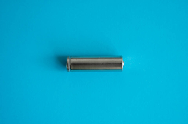 A single rechargeable battery on blue background. Silver alkaline AA battery for different device. Energy. - Foto, imagen