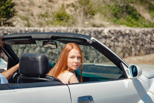 Couple enjoying a drive in a convertible in summer road. Friends going on holidays. Italian vacation serpentine roads, a redheaded woman and a beautiful young man - Fotoğraf, Görsel