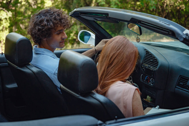 Couple enjoying a drive in a convertible in summer road. Friends going on holidays. Italian vacation serpentine roads, a redheaded woman and a beautiful young man - Фото, зображення