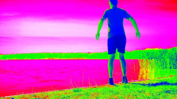 Deportista adulto corriendo y estirando en pantalla de visión térmica. Emisión de calor de la naturaleza y calentar el cuerpo masculino. Bahía del lago con playa de arena - Metraje, vídeo