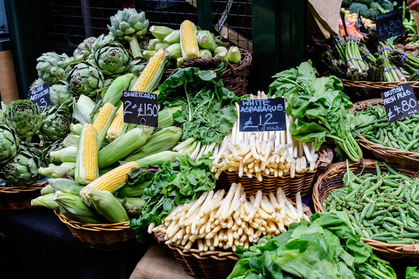 Зеленые органические овощи, выставленные на продажу на рынке уличной еды, с названиями на английском языке, артишоки, белая спаржа, сладкая кукуруза, британский горох, зеленая спаржа и свекольные листья с фермы - Фото, изображение