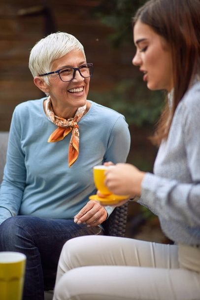 old cheerful mother and young adult daughter talking, drinking coffee - Foto, Imagen