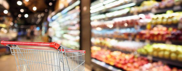 supermercado tienda de comestibles con estantes de frutas y verduras fondo desenfocado interior con carro de la compra rojo vacío - Foto, Imagen