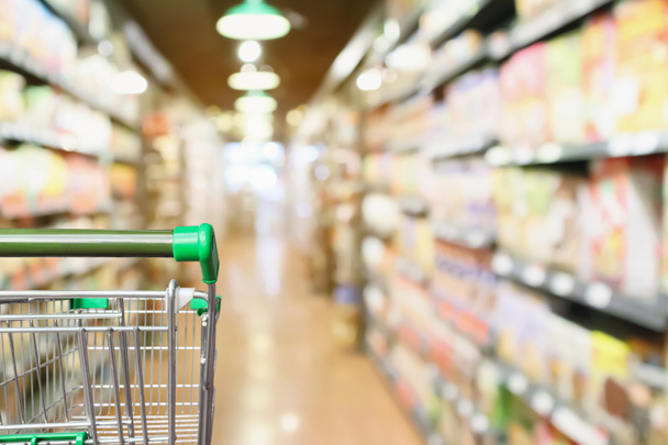 Empty green supermarket shopping cart with abstract blur grocery store aisle defocused background - Photo, Image