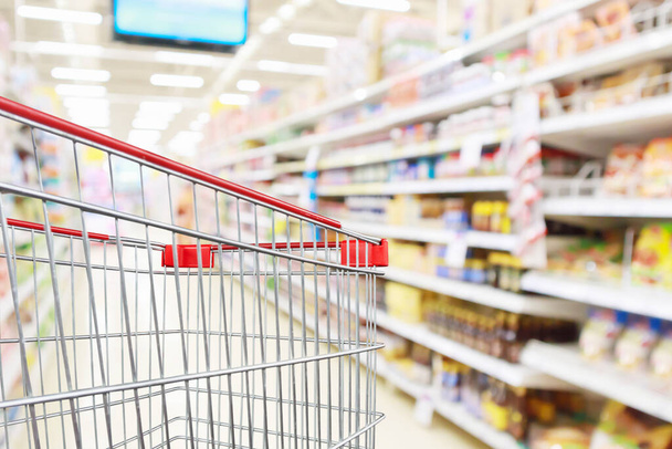 Empty shopping cart with abstract blur supermarket discount store aisle and product shelves interior defocused background - Fotoğraf, Görsel