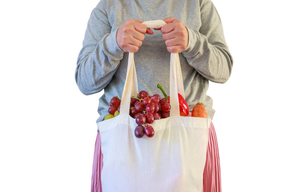 Vrouw houden eco-vriendelijke herbruikbare boodschappentas gevuld met volledige verse groenten en fruit kruideniersproduct geïsoleerd op witte achtergrond met clipping pad - Foto, afbeelding