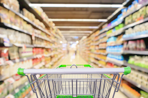 shopping cart in supermarket aisle with product shelves interior defocused blur background - Photo, Image