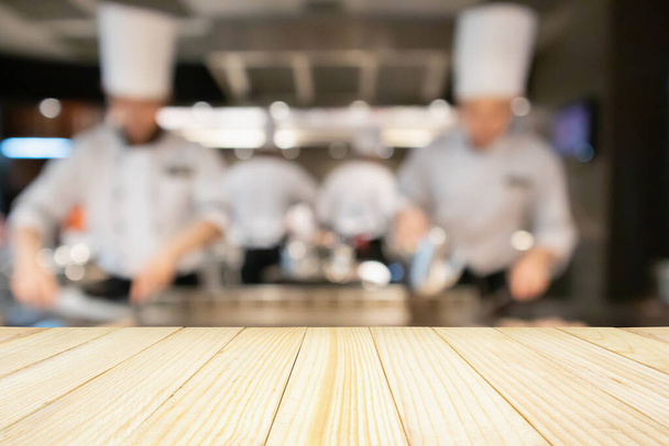 Leere Holztischplatte mit Koch in Restaurantküche verschwommener defokussierter Hintergrund - Foto, Bild