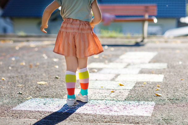 Κοντινό πλάνο των ποδιών του μικρού κοριτσιού που παίζει κουτσό παιχνίδι που με πολύχρωμα κιμωλίες στην άσφαλτο. Ένα μικρό ενεργό παιδί πηδάει σε παιδική χαρά σε μια ηλιόλουστη μέρα. Θερινές δραστηριότητες για παιδιά. - Φωτογραφία, εικόνα