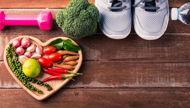Top view of various fresh organic fruit and vegetable in heart plate and sports shoes, dumbbell and water, studio shot on wooden gym table, Healthy diet vegetarian food concept, World food day - Fotoğraf, Görsel