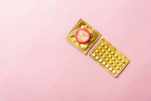 World sexual health or Aids day, condom on wrapper pack and contraceptive pills blister hormonal birth control pills, studio shot isolated on a pink background, Safe sex and reproductive health concept - Foto, afbeelding