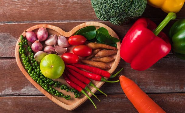 Welternährungstag, Draufsicht auf verschiedene frische Bio-Früchte und -Gemüse im Herzteller mit Kopierraum, Studioaufnahme auf Holztisch, Gesundes vegetarisches Ernährungskonzept - Foto, Bild
