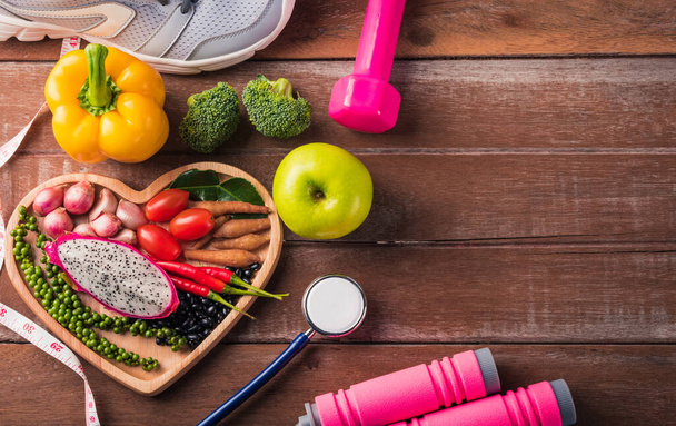 Top view of fresh organic fruit and vegetable in heart plate, shoes, sports equipment and doctor stethoscope, studio shot on wooden gym table, Healthy diet vegetarian food concept, World food day - Foto, immagini