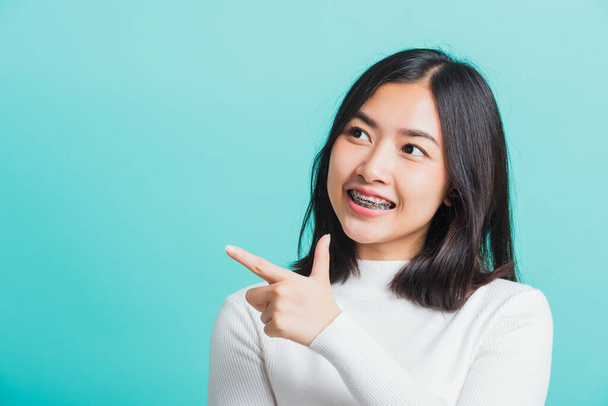 Portrait of Asian teen beautiful young woman smile have dental braces on teeth laughing point finger side away blank copy space, studio shot isolated on blue background, medicine and dentistry concept - Фото, зображення