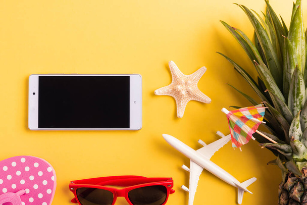 Celebrate Summer Pineapple Day Concept, Top view flat lay of funny pineapple, sunglasses, model plane, and smartphone blank screen, isolated on yellow background, Holiday summertime in tropical - Photo, Image