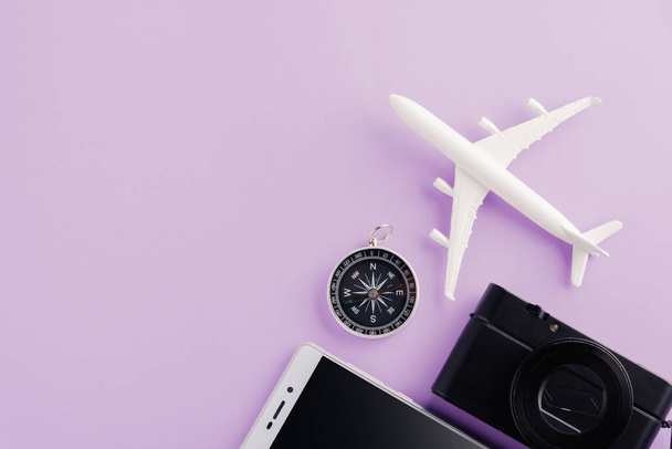 World Tourism Day, Top view of minimal model plane, airplane, starfish, alarm clock, compass, camera and smartphone, studio shot isolated on a purple background, accessory flight holiday concept - Foto, imagen