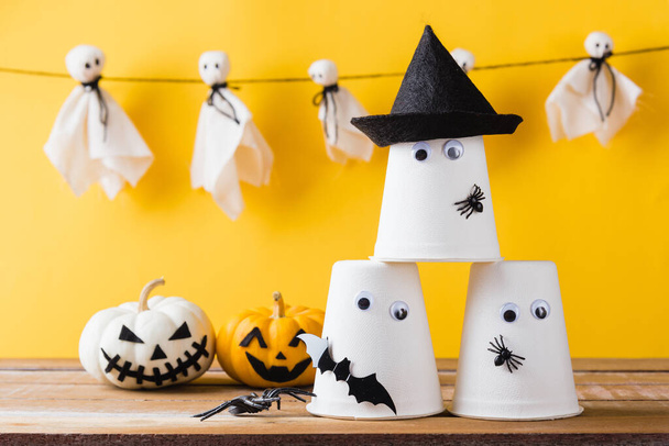 Funny Halloween day decoration party, Baby cute white ghost crafts scary face hanging and halloween crafts paper cup ghost on wood, studio shot isolated, Happy holiday DIY handicraft concept - Zdjęcie, obraz