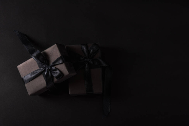 Black Friday sale shopping concept, Top view of gift box wrapped in black paper and black bow ribbon, studio shot on black background - Фото, зображення