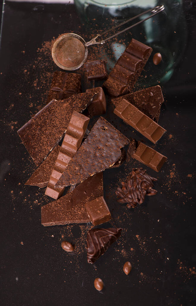 Zerbrochene Schokoladenstücke und Kakaopulver auf Holzgrund - Foto, Bild