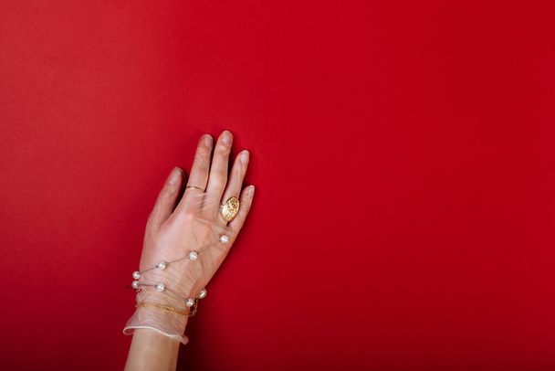 Fashion art χέρι γυναίκα στο γάντι προστασία από COVID-19 με κοσμήματα που απομονώνονται σε κόκκινο φόντο. - Φωτογραφία, εικόνα