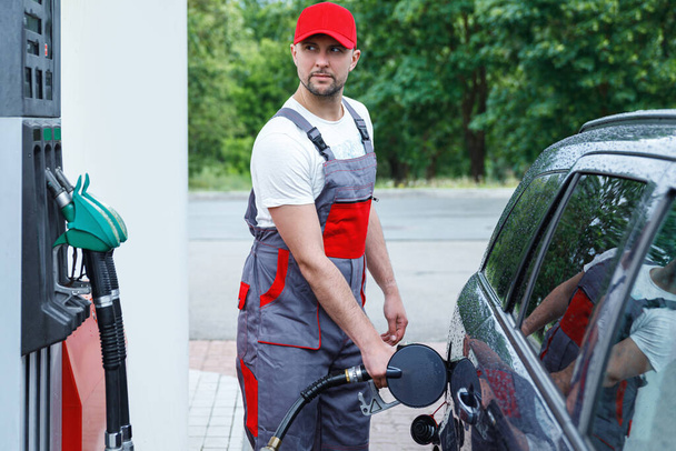 Filling station attendant with a fuel nozzle in his hands filling tank of clients car. - Fotografie, Obrázek