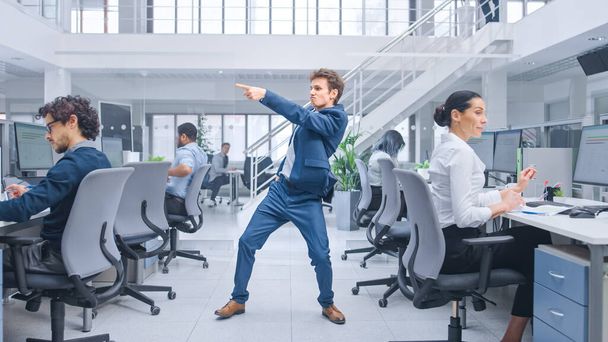 Young Happy and Cheerful Handsome Business Manager Wearing a Suit and Tie Dancing in the Office. Diverse and Motivated Business People Work on Computers in Modern Open Office. - 写真・画像