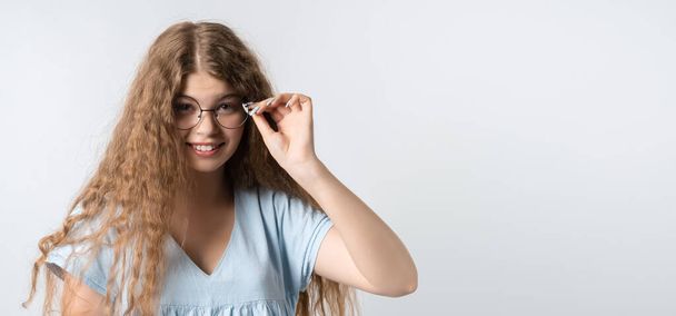 Retrato de menina moderna carismática com cabelos longos encaracolados em roupas leves casuais e usa óculos redondos posando isolado no fundo da parede branca. Conceito de estilo de vida. Copiar espaço para o seu texto - Foto, Imagem