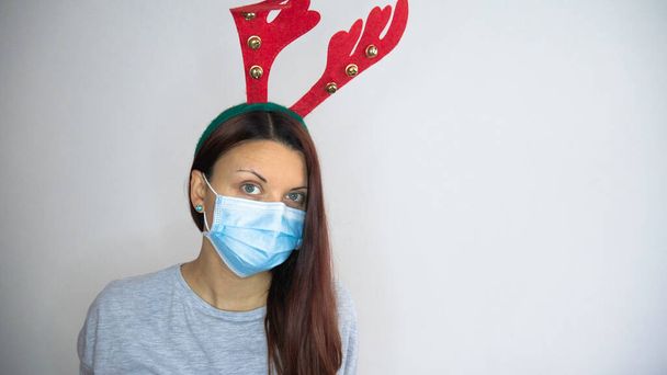 Frau mit Schutzmaske gegen Coronavirus und Hirschhörner-Stirnband. Weihnachten und Neujahr. Kopierraum für Text. - Foto, Bild
