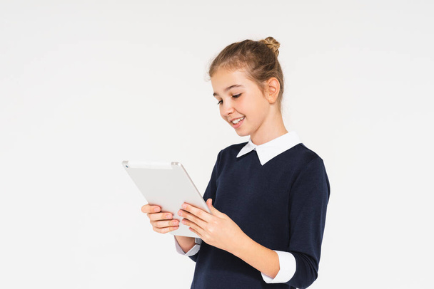 Mignon sourire adolescent fille en uniforme scolaire avec tablette dans les mains isolées sur fond blanc - Photo, image