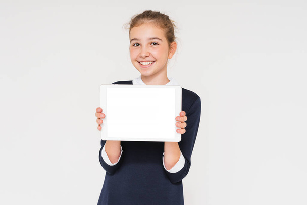 Linda chica adolescente sonriente en uniforme escolar con tableta en las manos aisladas sobre fondo blanco, maqueta - Foto, Imagen