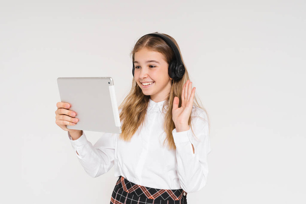 Cute smiling teen girl in school uniform with headphones and tablet in her hands isolated on white background - Photo, Image