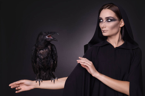 Mysterious witch with raven on dark background - Valokuva, kuva