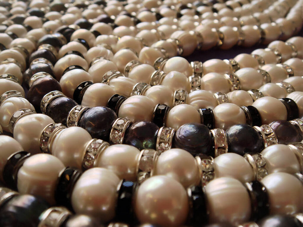 Primo piano di perle naturali di diversi colori: bianco avorio iridescente e grigio pavone con distanziali in strass fissati su corde per collane e bracciali o qualsiasi altra creazione di gioielli personalizzati - Foto, immagini